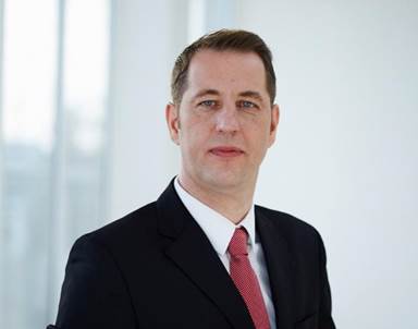 A person wearing a suit and tie smiling at the camera
Description automatically generated
